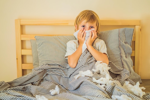 Un garçon malade tousse et s'essuie le nez avec des lingettes Enfant malade avec fièvre et maladie au lit