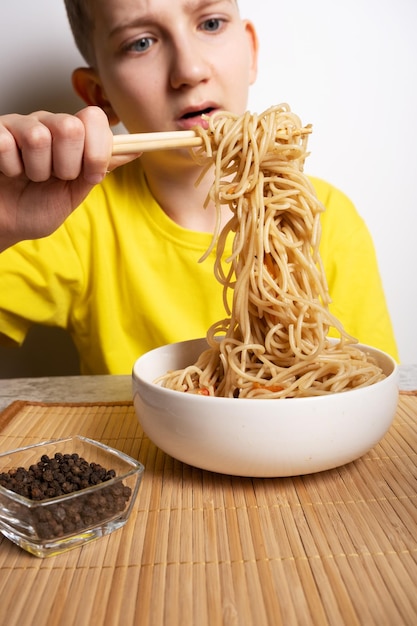 Un garçon mange des nouilles japonaises avec des baguettes Mise au point sélective sur les nouilles un plat asiatique