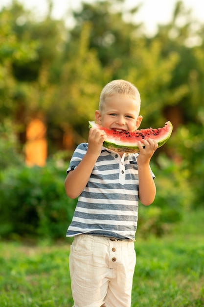 Le garçon mange de la pastèque à l'extérieur. vacances d'été à la campagne.