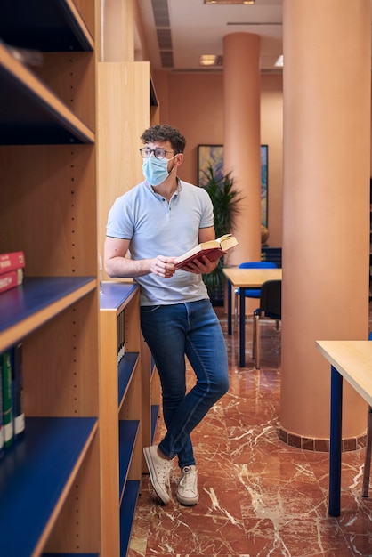 Un garçon avec un masque est debout dans une bibliothèque regardant par la fenêtre