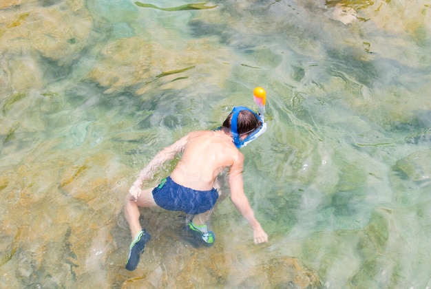 Un garçon avec un masque de natation nage dans un lac de montagne, regarde en bas