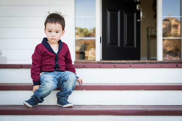 Un garçon mélangé mélancolique assis sur les marches du porche