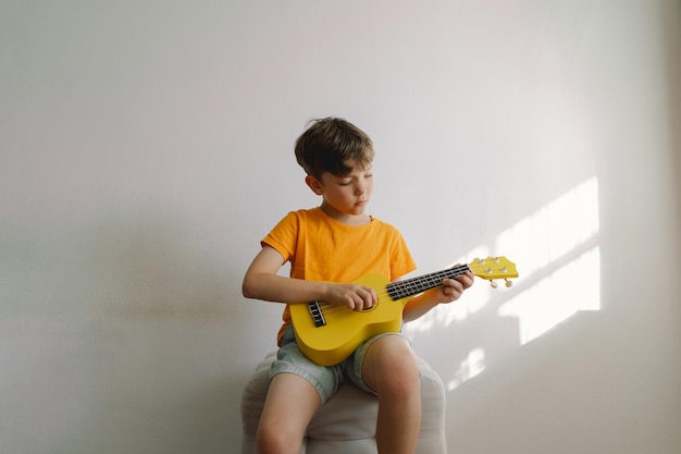 Un garçon mignon apprend à jouer de la guitare ukulélé jaune dans une maison confortable