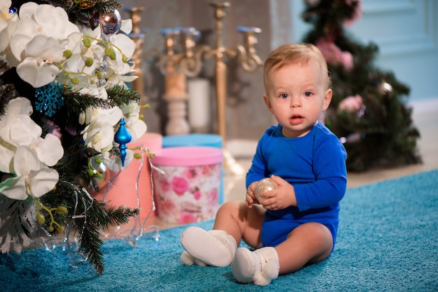 Garçon mignon assis sur le tapis près de sapin de Noël