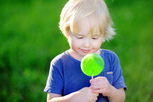 Garçon mignon bambin avec grosse sucette verte. Enfant mangeant des friandises sucrées. Bonbons pour les jeunes enfants. Plaisirs d&#39;été en plein air