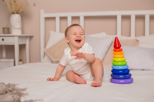 Garçon mignon bambin sourit assis sur le lit avec une pyramide multicolore