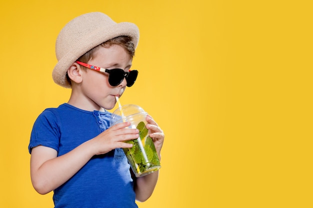 Un garçon mignon boit un cocktail Mojito dans une tasse en plastique.