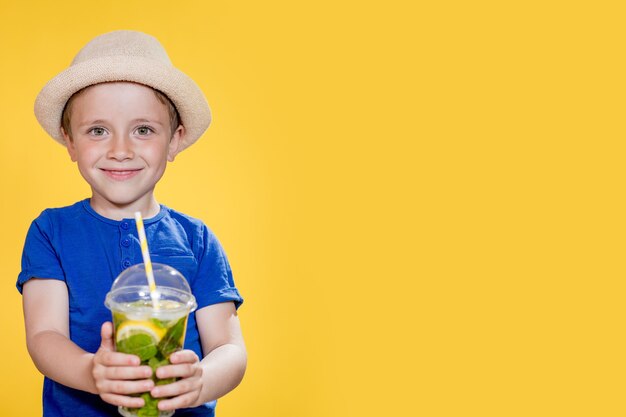 Un garçon mignon boit un cocktail Mojito dans une tasse en plastique.