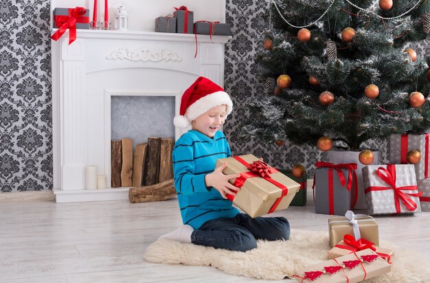 Garçon mignon en bonnet de Noel déballant des cadeaux de Noël