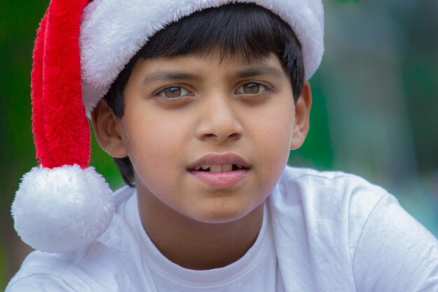 Photo un garçon mignon avec une casquette de père noël et un t-shirt blanc souriant joyeusement et regardant la caméra