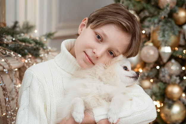 garçon mignon avec un chien dans ses bras dans un pull léger sur le mur d'un arbre de Noël