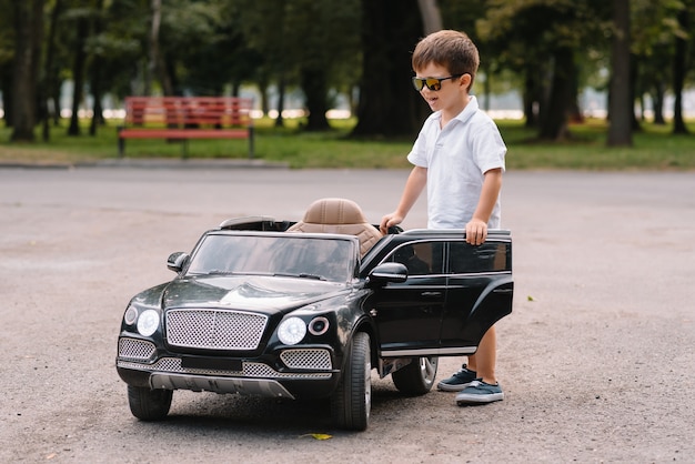 Garçon mignon à conduire une voiture électrique noire dans le parc