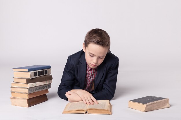 Un garçon mignon en costume se trouve et lit un livre sur un fond blanc.