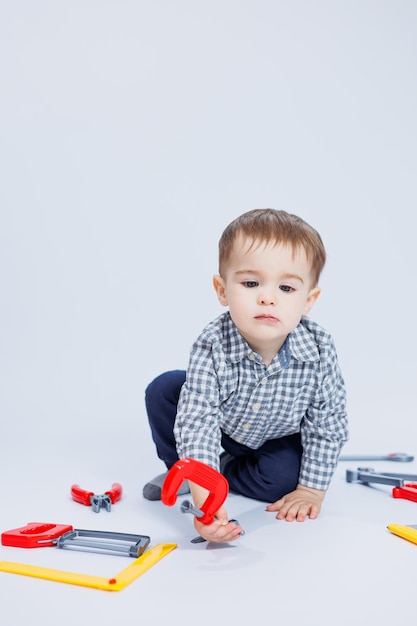 Un garçon mignon dans une chemise à l'image d'un constructeur sur fond blanc Apprentissage de l'enfance jeux de travail imitation de carrière Petit assistant de papa