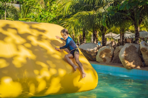 Un garçon mignon dirige un parcours d'obstacles gonflable dans la piscine