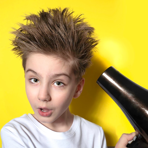 Garçon mignon émotionnel avec une coiffure joyeuse posant sur le fond du mur jaune