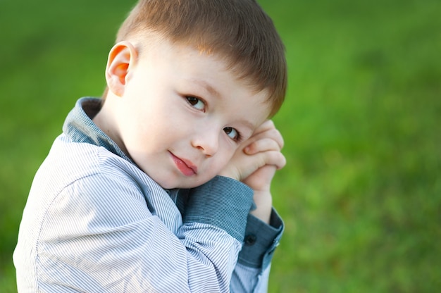 Garçon mignon est assis sur l'herbe verte. Il attend. enfants heureux