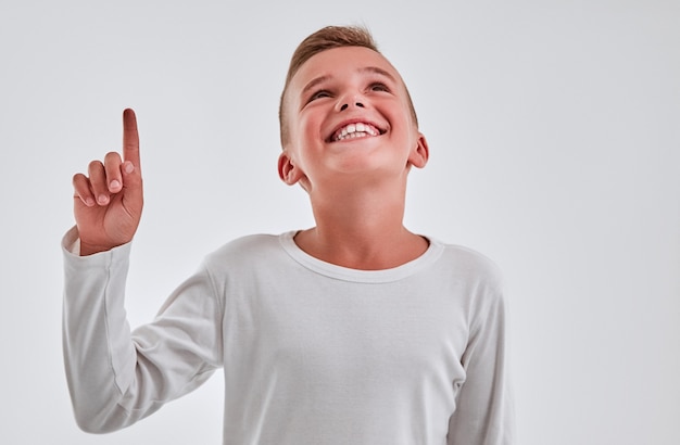 Photo un garçon mignon sur fond gris pointe avec sa main, lève les yeux et sourit