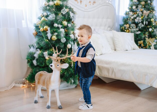 Garçon Mignon Avec Gros Cerf Jouet. Enfant Sur Le Fond D'une Salle De Noël Décorée. Vacances Du Nouvel An. Noël Et Nouvel An.