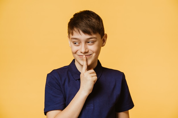 Garçon mignon habillé en tenue décontractée sur un mur jaune isolé demandant à être calme avec le doigt sur les lèvres en regardant de côté Silence et concept secret.