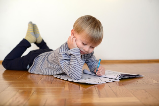 un garçon mignon lit le livre par terre à la maison