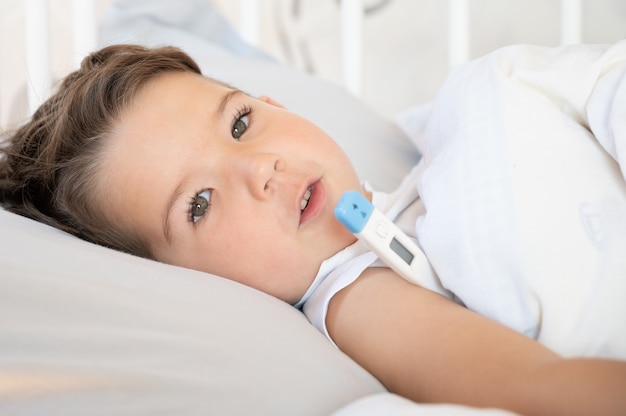 Un garçon mignon malade se trouve au lit avec un thermomètre. Notion de médecine. photo de haute qualité