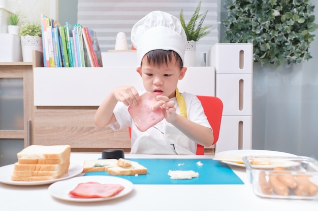 Garçon mignon portant une toque et un tablier préparant des sandwichs