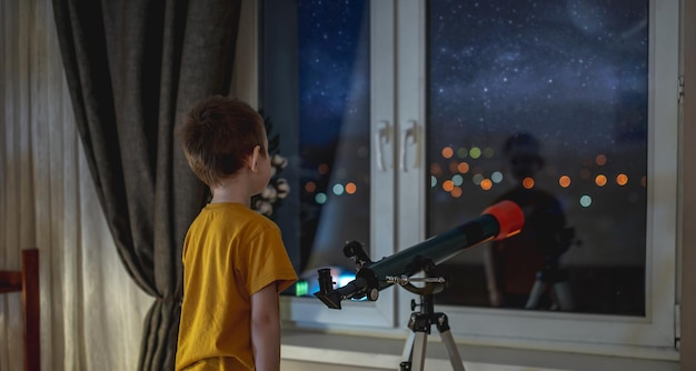 Un garçon mignon regarde à travers un télescope dans le ciel étoilé de la nuit La passion des enfants pour l'exploration spatiale