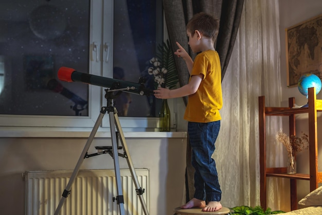 Un garçon mignon regarde à travers un télescope dans le ciel étoilé de la nuit La passion des enfants pour l'exploration spatiale