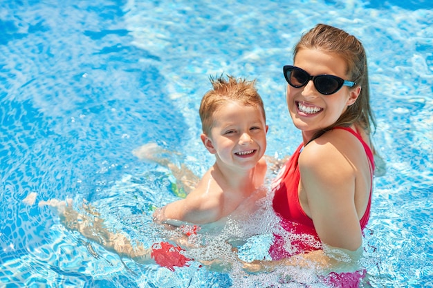 garçon mignon avec sa mère jouant dans une piscine d'eau pendant l'été