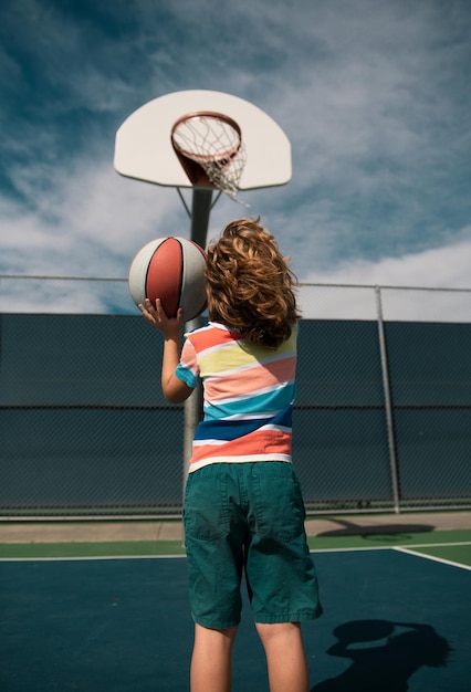 Un garçon mignon et souriant joue au basket. Des enfants actifs apprécient le jeu en plein air avec le basket-ball, un sport pour enfants.