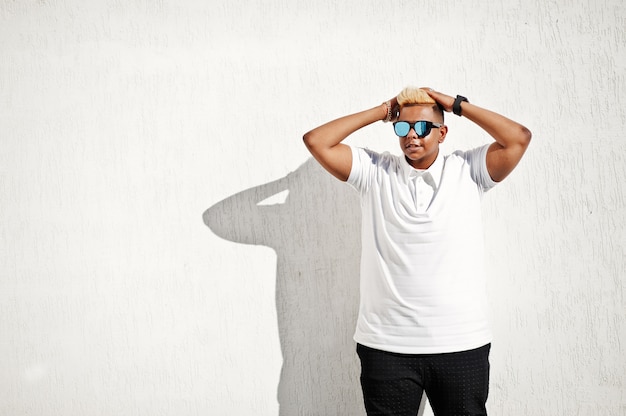 Garçon musulman arabe élégant avec à l'origine des cheveux et des lunettes de soleil posés dans les rues au toit contre le mur blanc.