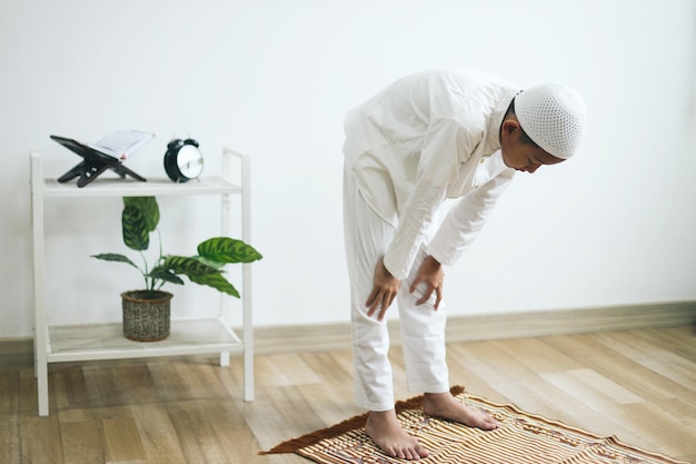 Un garçon musulman faisant la salat avec un geste de ruku sur le tapis de prière