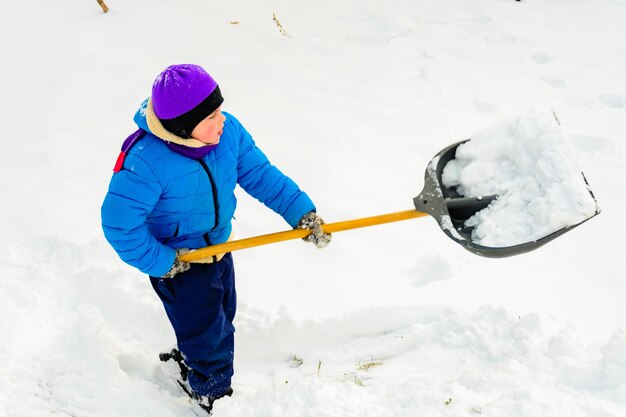 Le garçon nettoie la neige avec une pelle