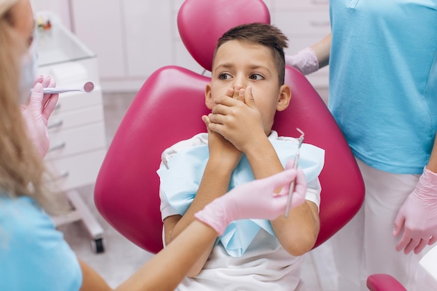 Le garçon a peur et ferme la bouche avec ses mains lors d'une visite chez le dentiste à la clinique dentaire