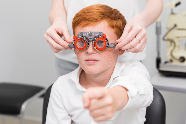 Garçon pointant vers la caméra pendant qu'une ophtalmologiste examine ses yeux