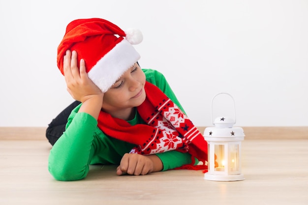 Garçon portant bonnet de Noel et écharpe d'hiver Enfant allongé sur le sol et regardant la lanterne de Noël