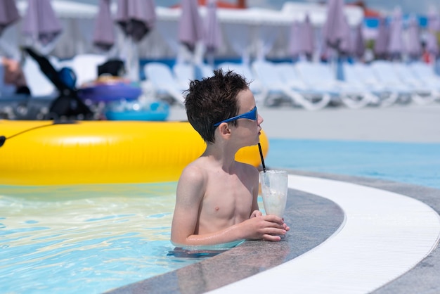 Photo un garçon portant des lunettes de soleil est debout dans une piscine avec de l'eau bleue et boit un milkshake resort summer