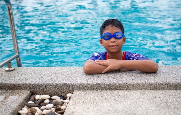 Le garçon portant des maillots de bain et des lunettes Sourire perché au bord de la piscine