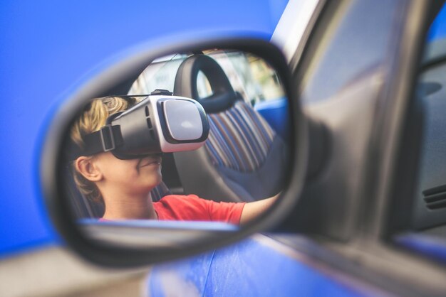 Un garçon portant un simulateur de réalité virtuelle dans une voiture se reflétant dans le miroir latéral