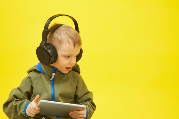 Un garçon porte des écouteurs tout en utilisant une tablette sur fond jaune