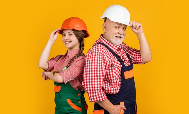 garçon positif et grand-père constructeur en casque sur fond jaune