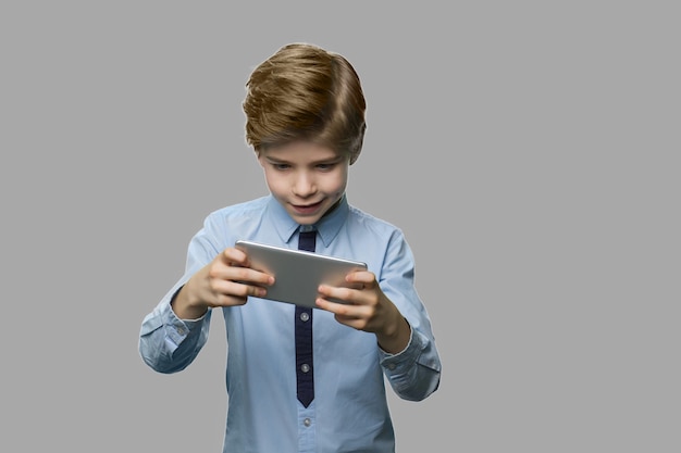 Garçon pré-adolescent jouant au jeu sur smartphone. Enfant excité jouant au jeu vidéo sur téléphone sur fond gris. Jeunesse, technologie, style de vie.