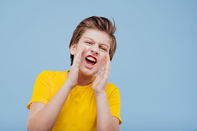 Garçon préadolescent énervant et hurlant en t-shirt jaune isolé sur mur bleu, espace copie