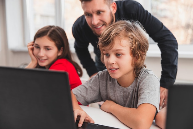 Garçon préadolescent intelligent montrant une solution de tâche sur un écran d'ordinateur portable à un enseignant masculin positif pendant la leçon de programmation dans une salle de classe moderne