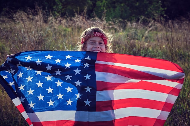 Un garçon préadolescent joyeux tenant le drapeau des États-Unis d'Amérique dans les mains tendues.