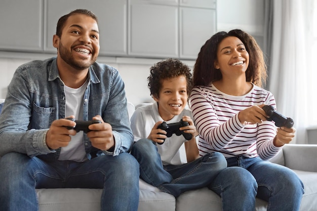 Un garçon préadolescent noir heureux jouant à des jeux vidéo avec ses parents à la maison.