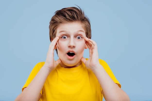 Garçon préadolescent surpris en t-shirt jaune isolé sur mur bleu, espace copie