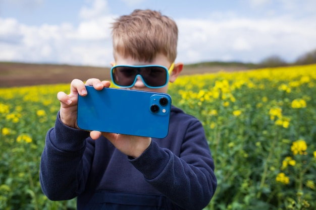 Le garçon prend des photos du paysage d'été du canola sur un smartphone