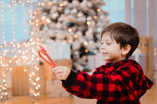 Un garçon en pyjama au caramel sous le sapin de Noël. Les bonbons du Nouvel An sont rouges.